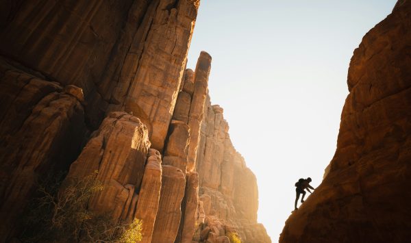 A rock climber in silhouette, climbing up through an orange canyon.